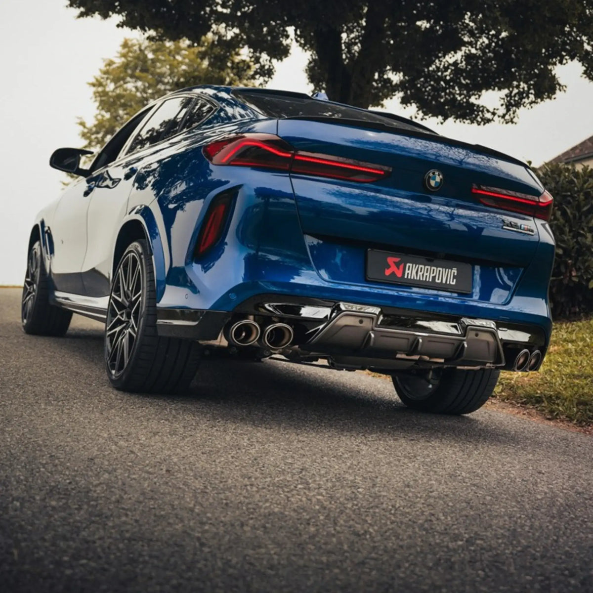 BMW X6 M captured on the road, featuring the Akrapovič Slip-On Line (Titanium) exhaust installed, rear angle emphasizing the carbon/titanium tailpipes.
