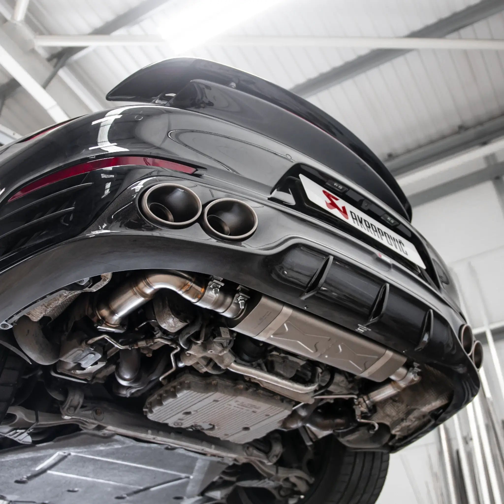 Porsche 911 Turbo S 991.2 on a lift in the PERON Performance workshop, showcasing the Akrapovic exhaust system and carbon diffuser.