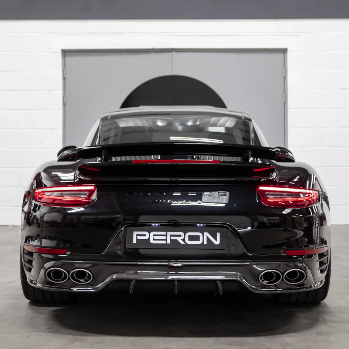 Rear straight-on shot of a Porsche 911 Turbo S 991.2 parked in the PERON Performance workshop post-installation of the Akrapovic performance exhaust.