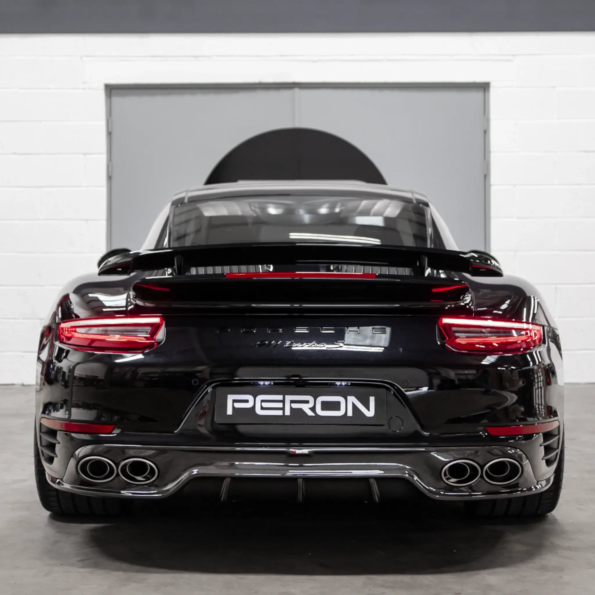 Rear straight-on shot of a Porsche 911 Turbo S 991.2 parked in the PERON Performance workshop post-installation of the Akrapovic performance exhaust.