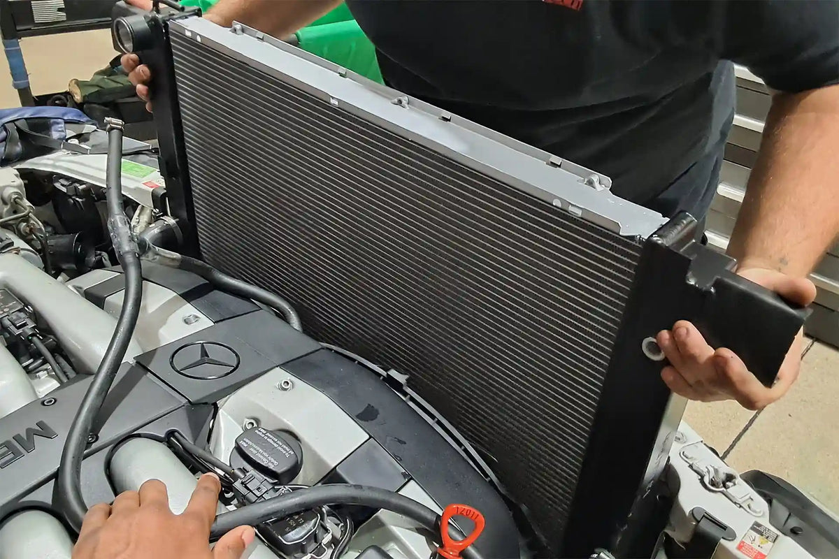 Technician fitting the CSF 7240 radiator into the engine bay of a Mercedes-Benz R129 V12