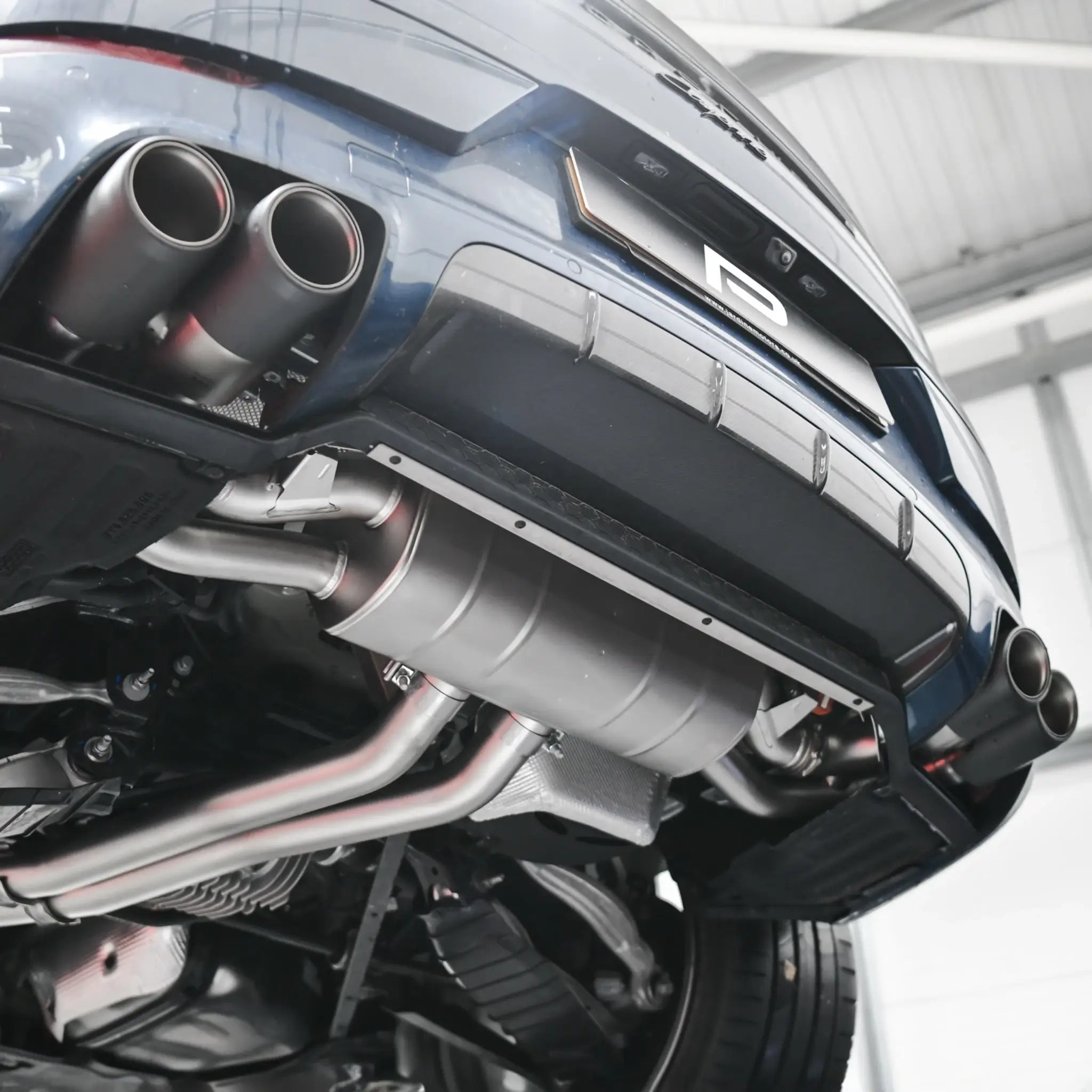 Underneath shot of installed Akrapovic Evolution Line exhaust on Cayenne 536.2, captured on the lift in PERON Performance Workshop.