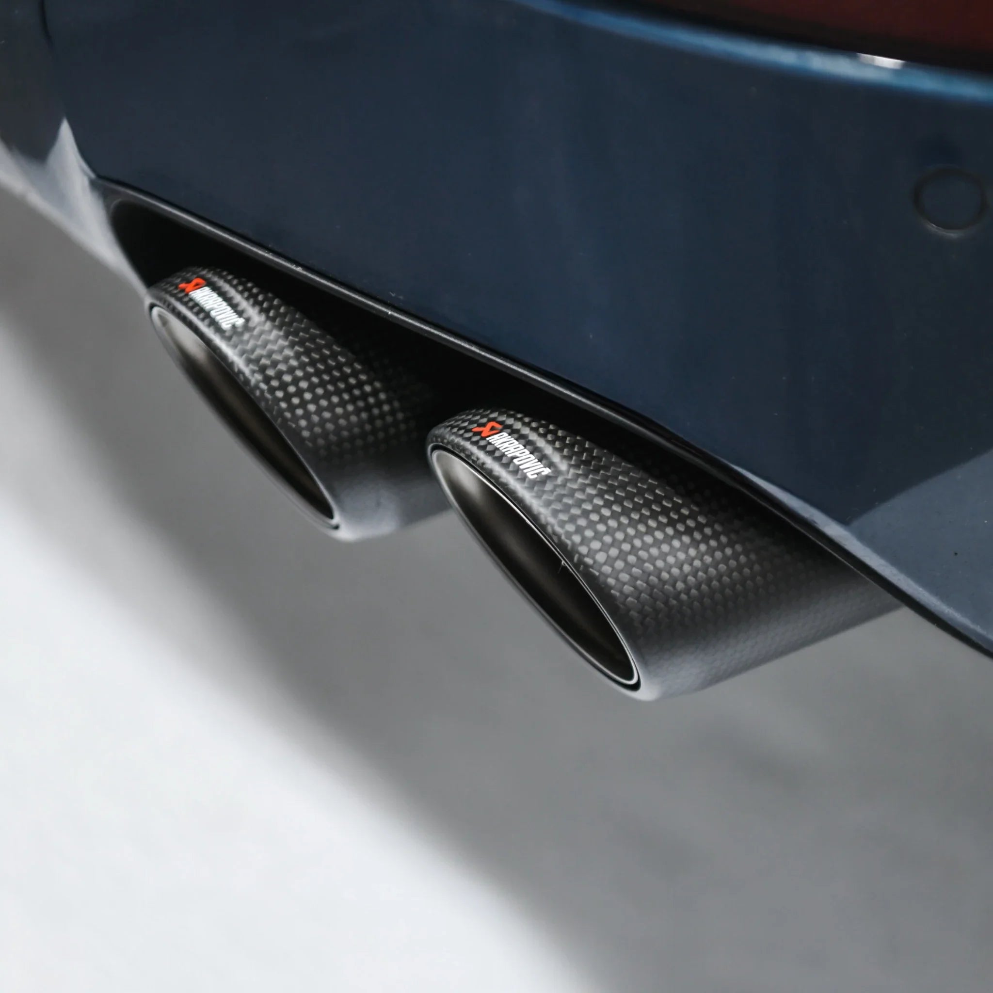 Detail shot of Akrapovic carbon tailpipe installed on Porsche Cayenne 536.2 in PERON Performance Workshop.