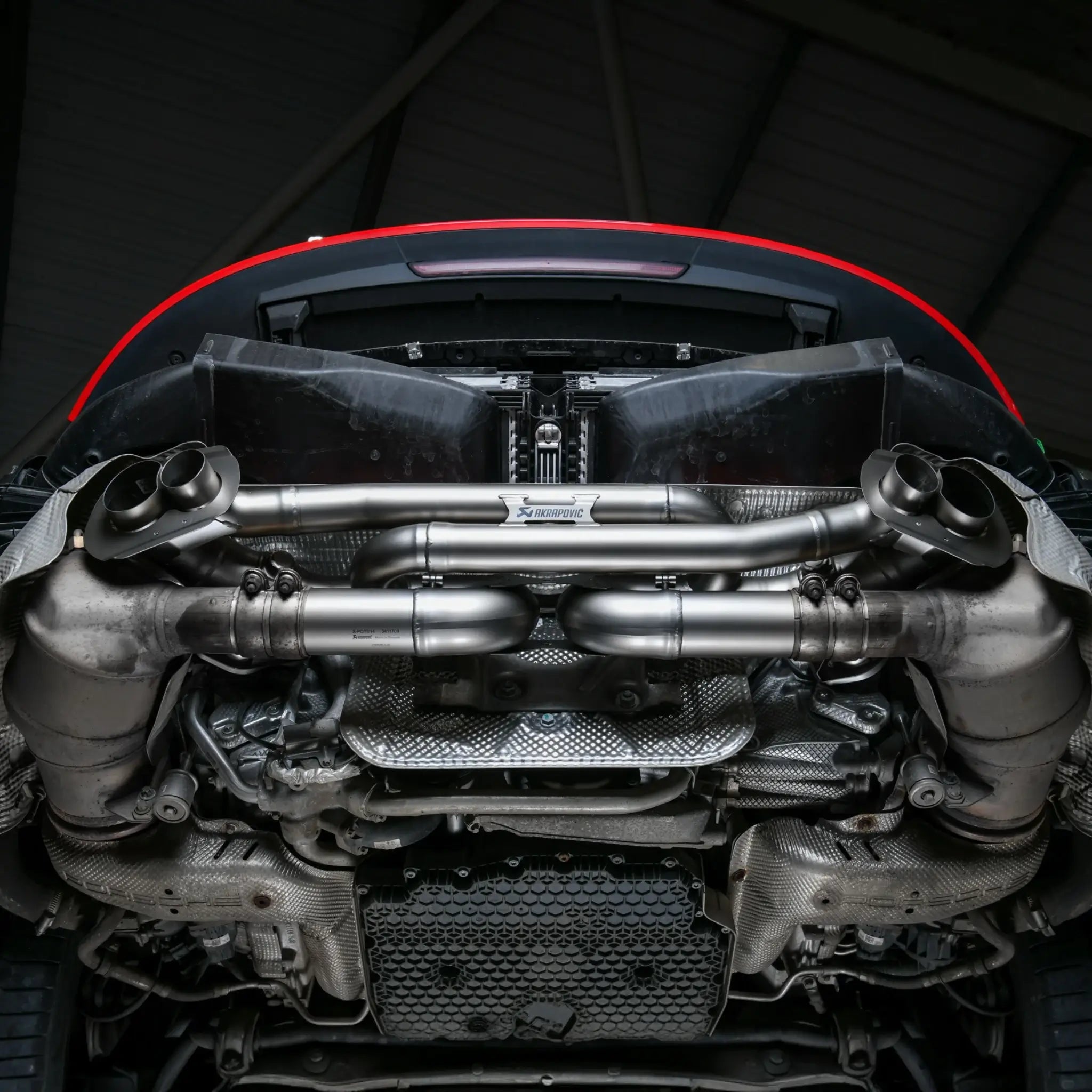 Akrapovic Slip-On Race Line exhaust installed on Porsche 911 Carrera 992 with bumper removed, on lift in Performance Workshop.